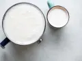 Un pot de lait chaud avec une fine peau de lait à la surface, à côté d'une tasse remplie de lait frais.