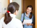 Assistente sociale sorridente, con fogli e penna, parla con una donna alla porta. Il suo lavoro è importante.