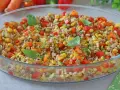 Insalata di farro colorata con mais, peperoni, zucchine e carote, guarnita con foglie di basilico fresco. Un piatto estivo e salutare.