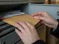 Ręce wyjmują kopertę z brązowego papieru ze skrzynki pocztowej, co może symbolizować nieodebranie nakazu zapłaty przez pozwanego.