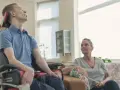 Młody mężczyzna na wózku inwalidzkim i kobieta siedzą w salonie.