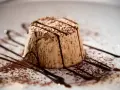 Delizioso parfait di mandorle, spolverato di cacao e decorato con scaglie di cioccolato fondente su un piatto bianco.