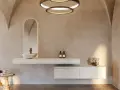 Une salle de bain nature aux murs texturés, avec un lavabo suspendu, un miroir arqué rétroéclairé et des touches végétales.