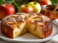 Un délicieux gâteau aux pommes, saupoudré de sucre glace, avec des pommes fraîches en arrière-plan.