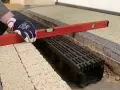 Rękawica z poziomicą sprawdza montaż odwodnienia liniowego w garażu.