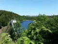 Idyllische Badeseen in Sachsen-Anhalt: Ein Stausee mit Damm und kleinem Haus, umgeben von grünen Wäldern unter blauem Himmel.