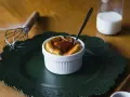 Delicioso souffle de vainilla con salsa de fresa, listo para disfrutar. A su lado, un batidor y un vaso de leche.