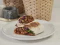Kebab zawinięty w tortillę, przekrojony na pół, z widocznym nadzieniem z mięsa, warzyw i sosu.