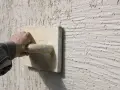 Main d'un artisan appliquant un enduit projeté texturé. Le prix au m2 de ce type de finition est souvent demandé.
