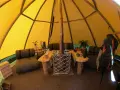 Mysig interiör i ett tipi-tält på Sorsele camping. Här finns sittplatser, ett bord och en kamin för värme.