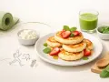 Zdrowe placki z serka wiejskiego, ozdobione truskawkami i miętą, obok zielonego smoothie i maty do ćwiczeń. Idealne na aktywny dzień!