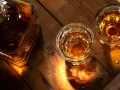 Butelka i dwa kieliszki z bursztynowym płynem, przypominającym koniak lub whisky, stoją na drewnianym blacie.