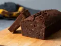 En saftig banankaka utan socker, med en skiva uppskuren. En övermogen banan ligger i bakgrunden, redo att förvandlas till denna goda banankaka.