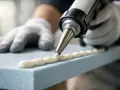 En person med handskar använder en fogpistol för att måla cellplast med ett vitt klister.