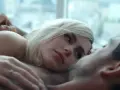 Blondynka i brunet leżą blisko siebie, ich ciała stykają się. Intymna scena, która sugeruje seks na scenie.