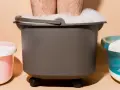 A person's legs are submerged in a foamy foot bath, part of a home foot detox setup with other foot spa machines.