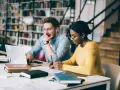 Studenti universitari collaborano a un progetto, immersi in libri e tecnologia.