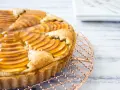 Deliciosa tarta de pera francesa, con peras laminadas y glaseado dorado, enfriándose sobre una rejilla de cobre.