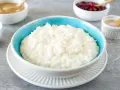 Cremiger Milchreis im blauen Schälchen, daneben Apfelmus, Kirschen und Zimt. Perfekt für ein einfaches Milchreis Rezept.