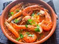 Deliciosa zarzuela de pescado con gambas, mejillones y cigalas en una cazuela de barro, adornada con perejil fresco.
