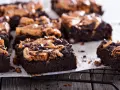 Pyszne brownie z bananami i masłem orzechowym, posypane czekoladowymi kropelkami, kuszą na czarnej kratce.