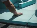 Mano che posiziona pannelli isolanti azzurri, materiali per cappotto termico, su membrana impermeabile.