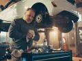 Mechanik wyciera ręce, podczas gdy samochód wisi na podnośniku, odsłaniając układ hamulcowy.