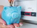 Ahorra con el plan renove calderas gas natural. Una mano deposita una moneda en una hucha cerdito azul junto a un contador de gas.
