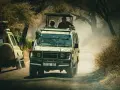 Dwa samochody terenowe jadące w pyle podczas tanzania safari. Ludzie stoją w otwartych dachach, obserwując dziką przyrodę.
