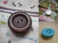 Gros plan sur un bouton à queue marron, prêt à être cousu sur un tissu orné de petites fourmis. Un autre bouton nacré est visible sur un tissu coloré.