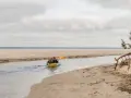 Dwie osoby płyną kajakiem po rzece Piaśnica, w kierunku morza. Piasek i chmury tworzą tło.