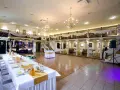 Elegancka sala weselna z długim stołem, ozdobionym złotą podkową. W tle bar i schody prowadzące na antresolę.