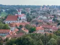 Widok na Wilno z wzgórza Giedymina. Czerwone dachy, białe kościoły i zielone drzewa tworzą malowniczy krajobraz.