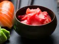 Miseczka z różowym imbirem do sushi, obok kawałek łososia i zielone wasabi.