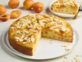 Saftiger aprikosenkuchen mit frischen aprikosen und Mandelblättchen, ein Stück bereits angeschnitten.