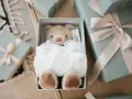 En mjuk nallebjörn i en presentbox, omgiven av fler presenter med ljusrosa band. En perfekt välkommen till världen present.
