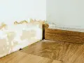 Dégâts sur un mur blanc dus à une infiltration d'eau, avec des traces de moisissure et de peinture écaillée près du sol et de la plinthe en bois.