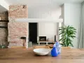 Salón con pared de ladrillo visto, mesa de madera con jarrones y planta.