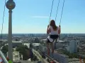 Frau schaukelt hoch über Alexanderplatz Berlin, mit Blick auf die Stadt und den Fernsehturm.