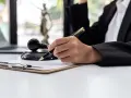 Ręka prawnika z piórem nad dokumentem, obok młotka sędziowskiego i Statuy Temidy. Nadzorca sądowy pracuje nad sprawą.