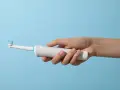 Dłoń trzyma białą szczoteczkę elektryczną. Czy można mieć szczoteczkę elektryczną w bagażu podręcznym? Tak, zazwyczaj można.
