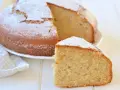Una fetta di soffice torta di banane mature, spolverata di zucchero a velo, accanto alla torta intera su un piatto bianco.