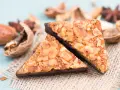 Zwei dreieckige Nussecken mit Schokoladenboden, bestreut mit gehackten Nüssen. Ein köstliches nussecken rezept zum Nachbacken.