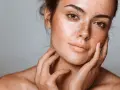 Visage d'une jeune femme aux taches brunes naturelles, ses mains caressant délicatement sa peau.