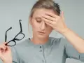 Donna con emicrania e dolore agli occhi, si tiene la fronte e in mano occhiali.