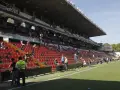 Puste trybuny stadionu Vallecas, z kilkoma osobami siedzącymi i stojącymi.