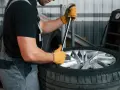 Mechanik w żółtych rękawicach używa klucza, by pokazać, jak zdjąć oponę z felgi.