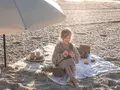 Dziewczynka na plaży pod parasolem, z owocami i ananasem. Idealne rzeczy, co zabrać na wakacje nad morze z dzieckiem.