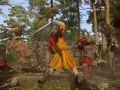 Combate en un bosque de Kingdom Come Deliverance. Un caballero con armadura lucha contra un guerrero con túnica amarilla, mientras un caballo se levanta en pánico. ¡Descubre los kingdom come deliverance trucos para sobrevivir!