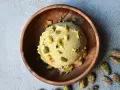 Cremoso helado de pistacho servido en un cuenco de madera, adornado con trozos de pistacho y acompañado de más pistachos enteros esparcidos alrededor.